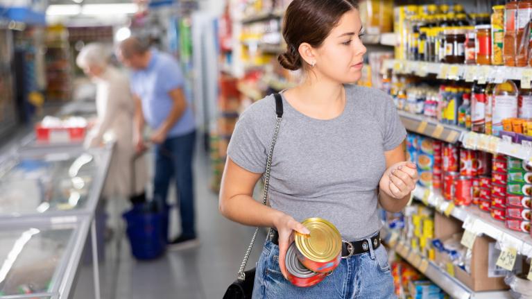 Junge Frau im Supermarkt mit Konservendosen in der Hand