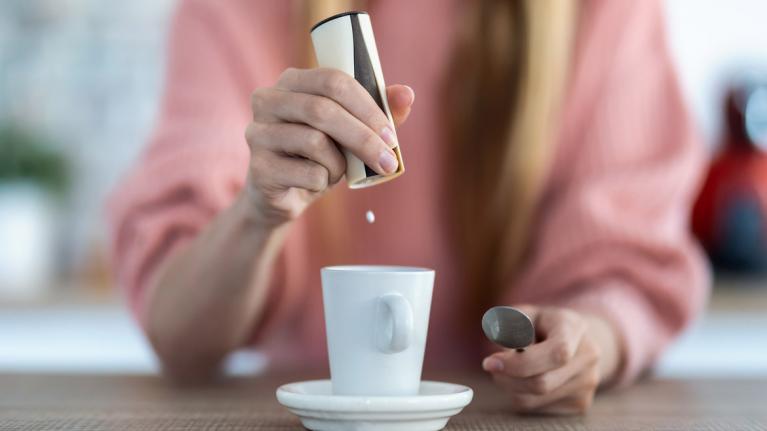 Frau gibt Süßstoff in Kaffeetasse