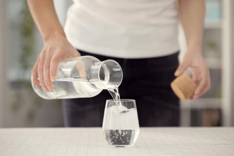 Frau gießt Wasser aus Karaffe in Glas