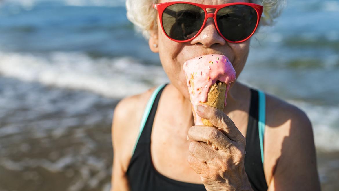 Ältere Frau mit Sonnenbrille isst Eis am Strand