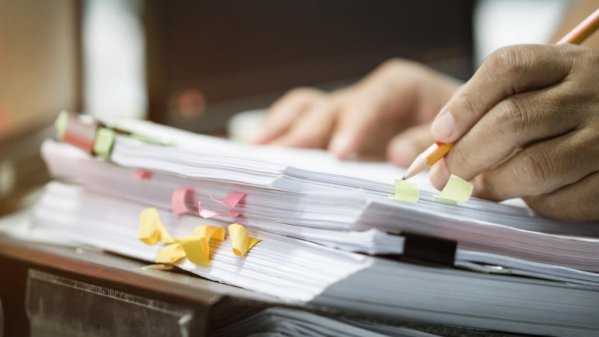 Aktenstapel mit Hand und Bleistift