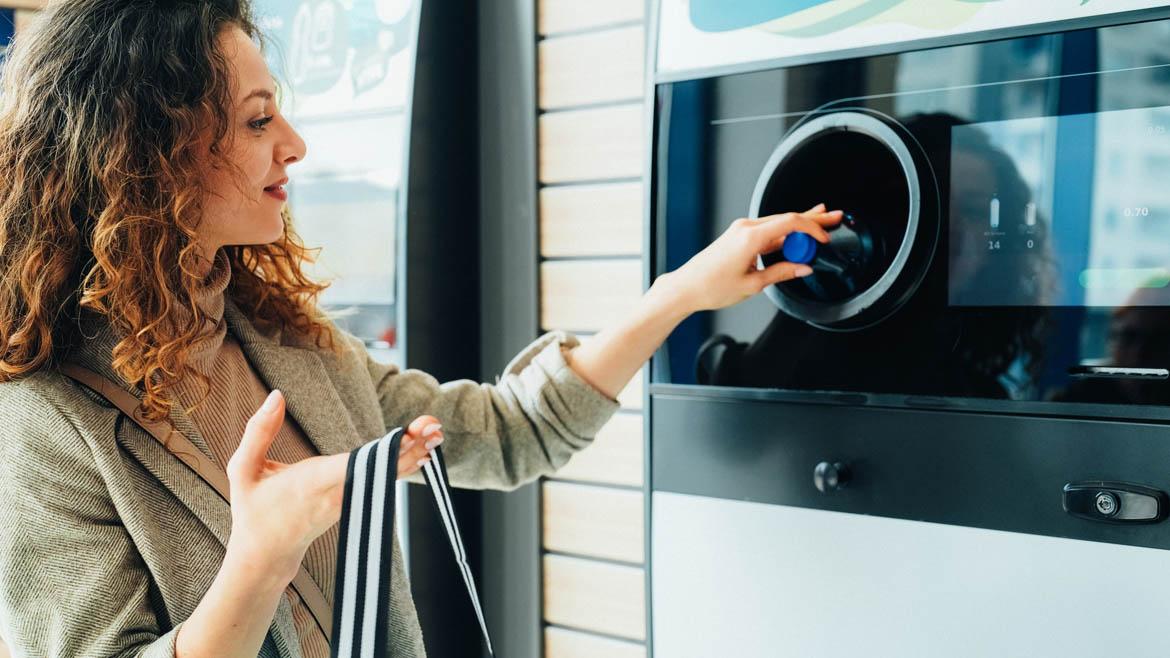 Frau gibt Flasche am Pfandautomaten zurück