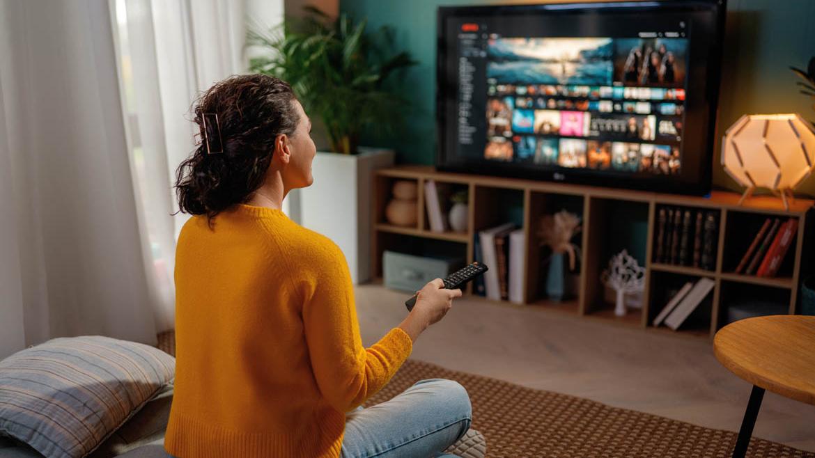 Frau mit Fernbedienung schaut auf Fernseher