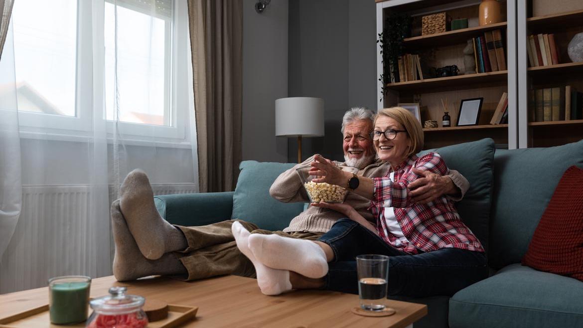 Paar sitzt auf Sofa und schaut Film mit Popcorn