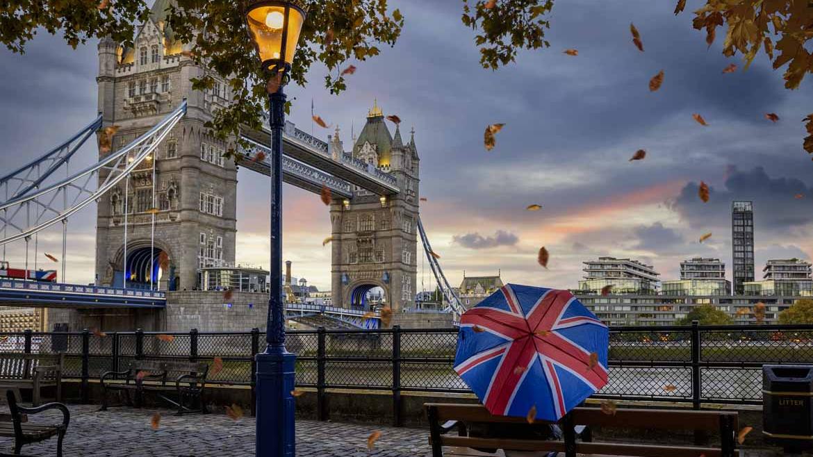 Person mit Regenschirm sitzt an Tower Bridge in London
