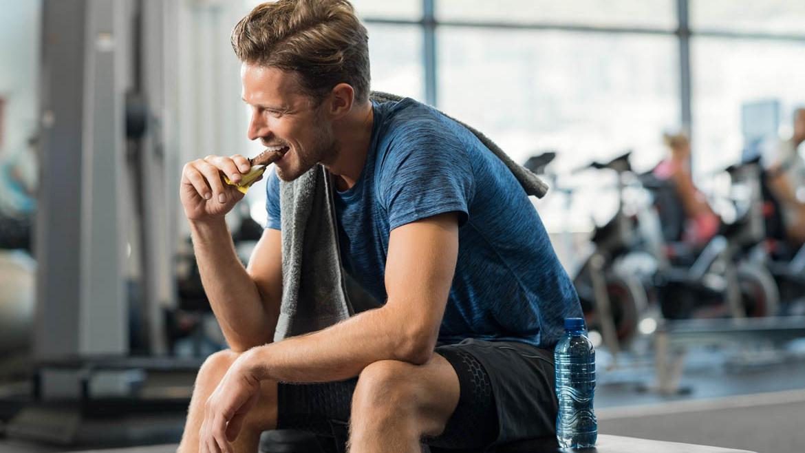 Sportler in Sportkleidung isst Energieriegel im Fitnessstudio