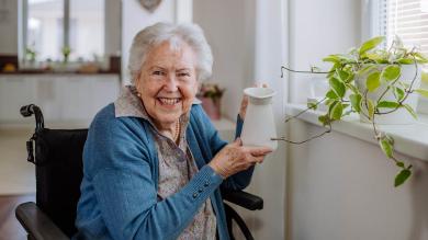 Ältere Frau im Rollstuhl mit Kanne in der Hand