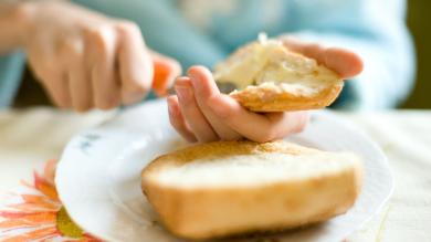 Person bestreicht ein Brötchen mit Margarine bzw. Butter