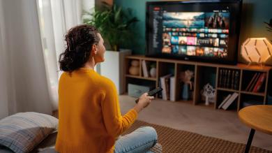 Frau mit Fernbedienung schaut auf Fernseher