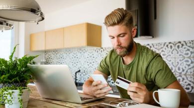 Junger Mann sitzt mit einer Kreditkarte vor dem Laptop