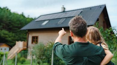 Mann mit Kind zeigt auf Haus mit Photovoltaikanlage