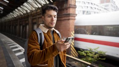 Mann am Bahnsteig mit Smartphone in der Hand; ICE im Hintergrund