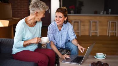 Eine ältere und eine jüngere Frau reden miteinander, daneben steht ein Laptop auf einem Tisch