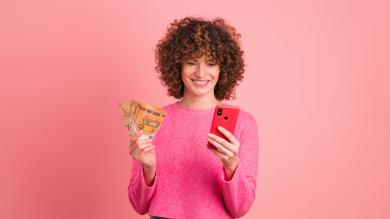 Frau vor rosa mit Geldscheinen und Handy in der Hand 