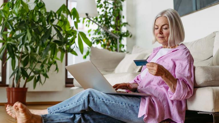 Ältere Frau mit Laptop und Kreditkarte in der Hand