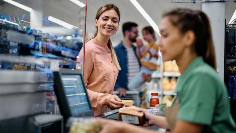 Junge Frau, die Lebensmittel an der Kasse bezahlt, während sie mit ihrer Familie im Supermarkt einkauft.