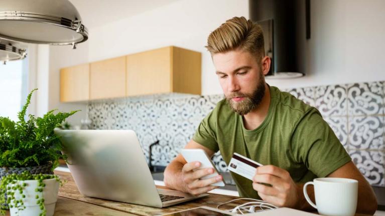 Junger Mann sitzt mit einer Kreditkarte vor dem Laptop