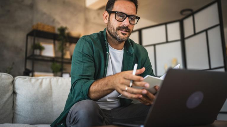 Mann schaut auf Laptop und macht Notizen