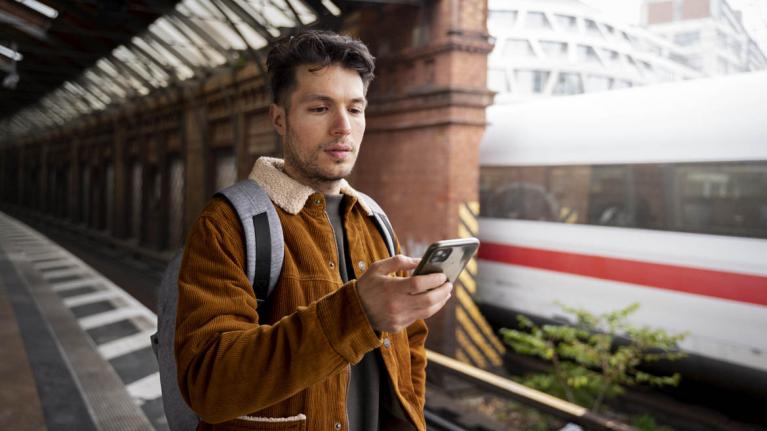 Mann am Bahnsteig mit Smartphone in der Hand; ICE im Hintergrund