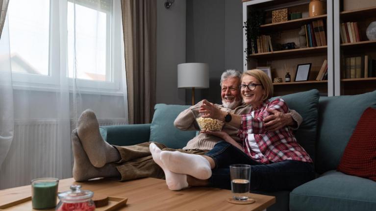 Paar sitzt auf Sofa und schaut Film mit Popcorn