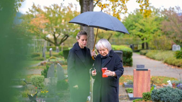 Zwei Frauen auf einem Friedhof mit einer Kerze in der Hand