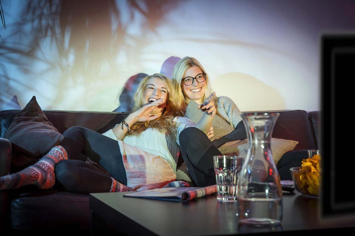 Zwei junge Frauen sitzen auf einem Sofa und schauen Fernsehen