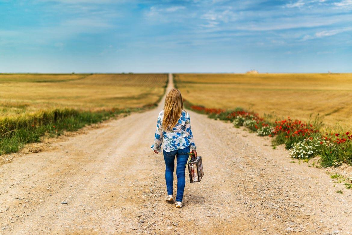 Frau mit Koffer in der Hand auf einem Feldweg