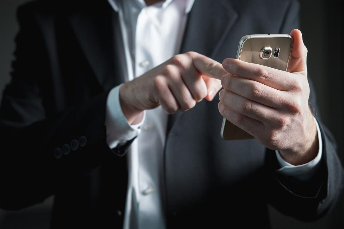 Mann in dunklem Anzug mit Smartphone in der Hand