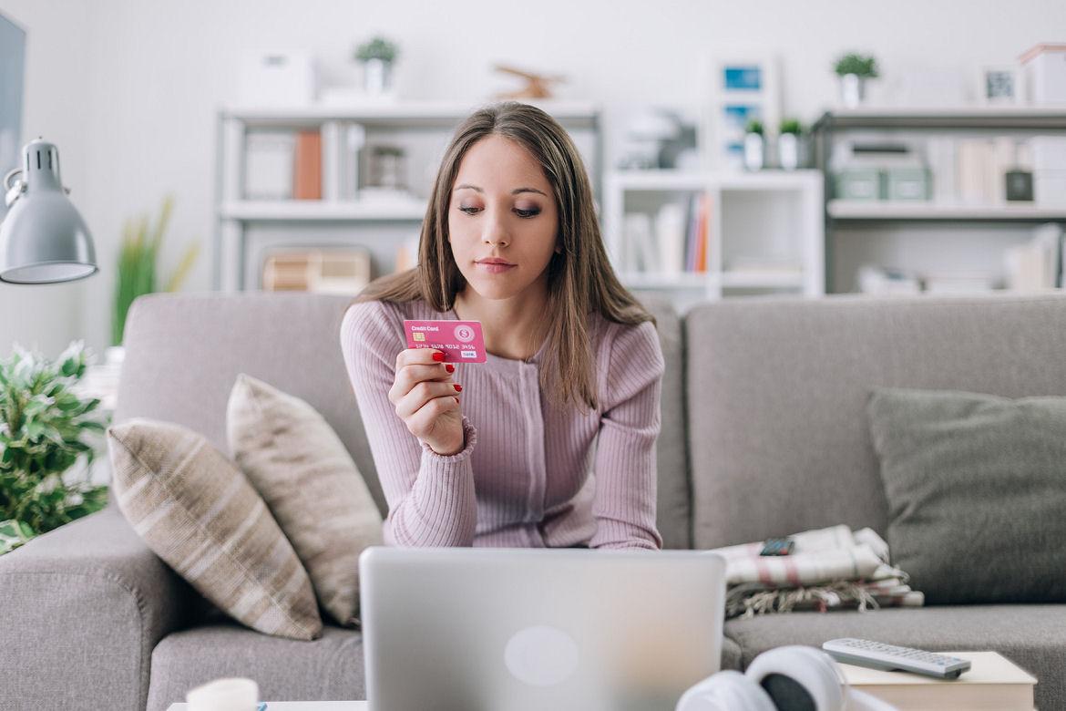 Junge Frau schaut beim Online-Shopping auf ihre Kreditkarte