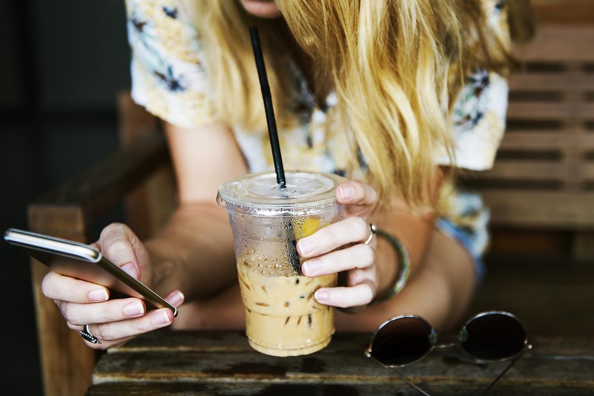 Frau die Kaffee trinkt und auf ein Smartphone schaut