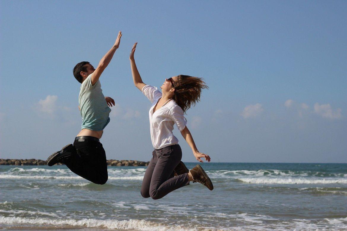 Zwei Menschen springen am Strand in die Luft und klatschen sich ab