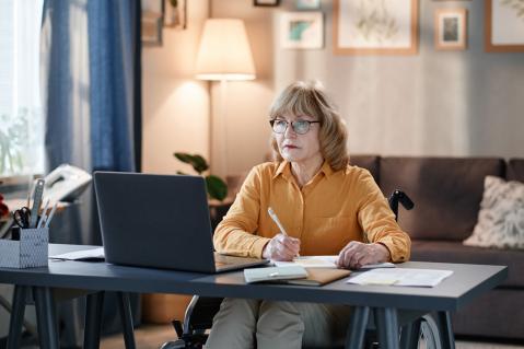 Ältere Frau schaut ernst auf Laptop und hat einen Stift in der Hand