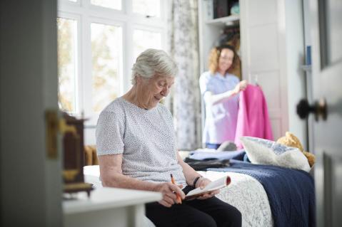 Ältere Frau sitzt auf einem Bett und hält Papier in der Hand