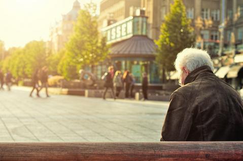 Älterer Mann sitzt auf Bank in Fußgängerzone