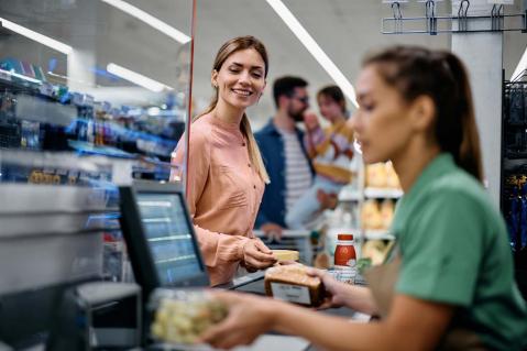 Junge Frau, die Lebensmittel an der Kasse bezahlt, während sie mit ihrer Familie im Supermarkt einkauft.