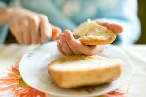 Person bestreicht ein Brötchen mit Margarine bzw. Butter