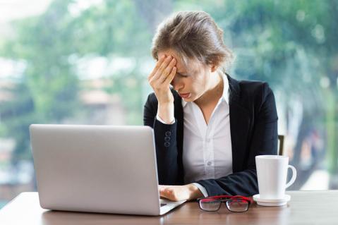 Frau an Laptop hält sich die Hand an den Kopf