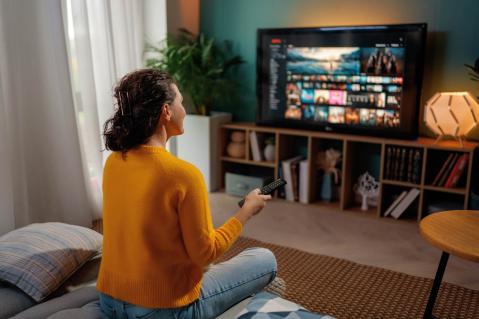 Frau mit Fernbedienung schaut auf Fernseher