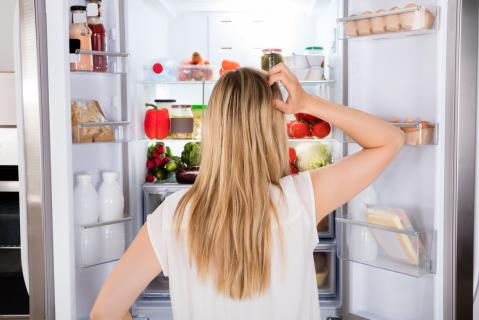Frau mit langen Haaren steht vor einem offenen Kühlschrank