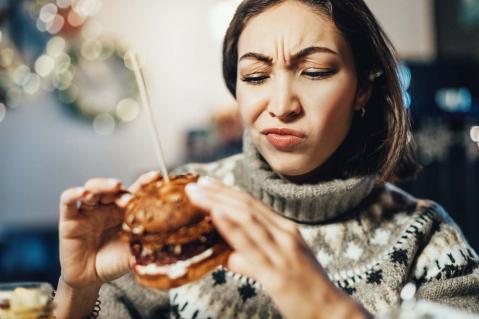 Junge Frau hält Burger in der Hand und schaut skeptisch