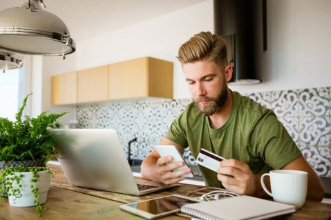 Junger Mann sitzt mit einer Kreditkarte vor dem Laptop