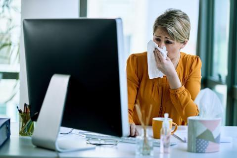 Kranke Frau mit Taschentuch am Computer