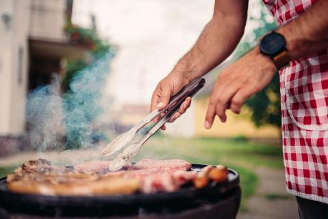 Person mit kariertem Hemd grillt Wurst