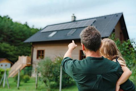 Mann mit Kind zeigt auf Haus mit Photovoltaikanlage