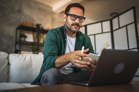 Mann schaut auf Laptop und macht Notizen