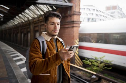 Mann am Bahnsteig mit Smartphone in der Hand; ICE im Hintergrund