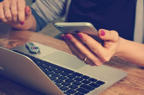 Frau mit Smartphone in der Hand vor einem Laptop