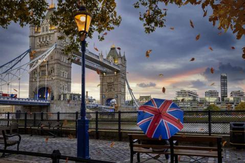 Person mit Regenschirm sitzt an Tower Bridge in London