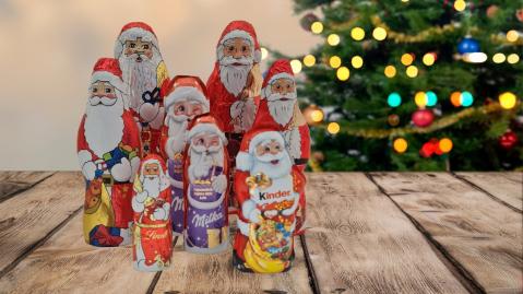 Schoko-Weihnachtsmaenner auf Holztisch mit Weihnachtsbaum im Hintergrund