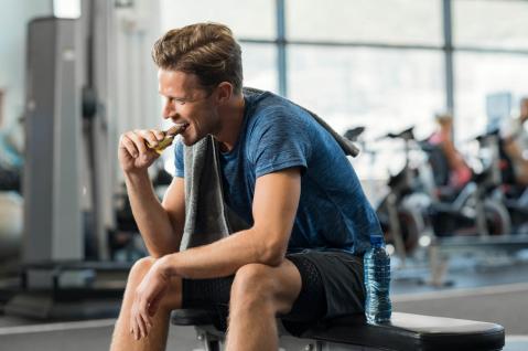 Sportler in Sportkleidung isst Energieriegel im Fitnessstudio